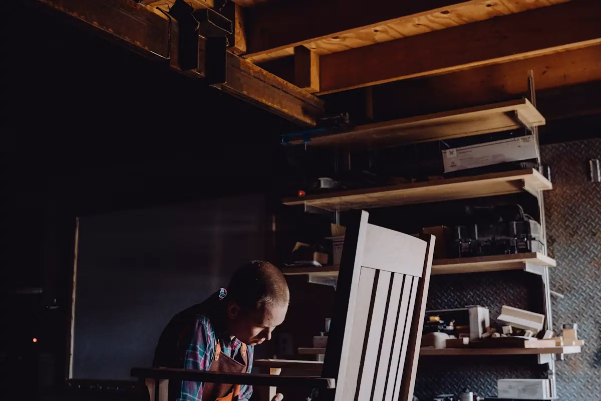 A person working on a wooden chair frame at a bench in a furniture workshop