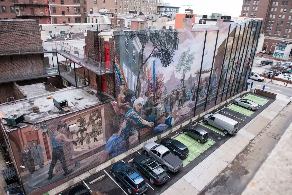 A large painted mural covering the side wall of a city building above a parking lot