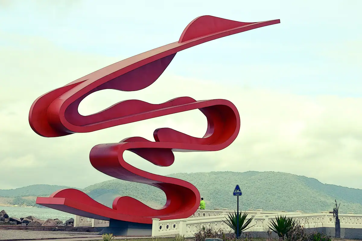 A large red-painted steel abstract sculpture standing on open grass in a city space