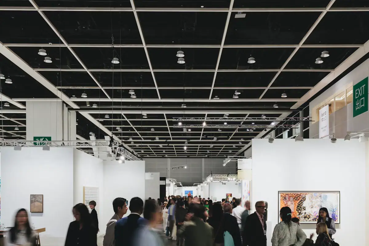 Visitors walking through a long, brightly lit exhibition hall hung with artworks