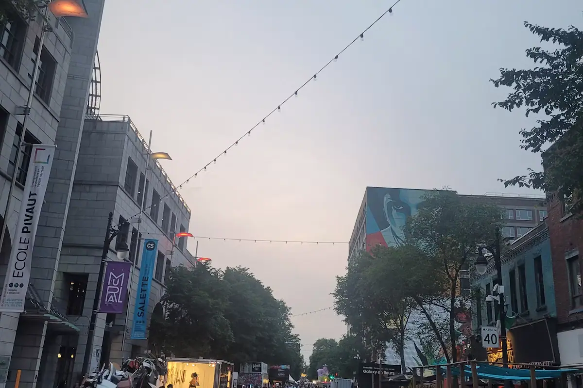 People walking along a pedestrian street of low buildings strung with lights in the evening
