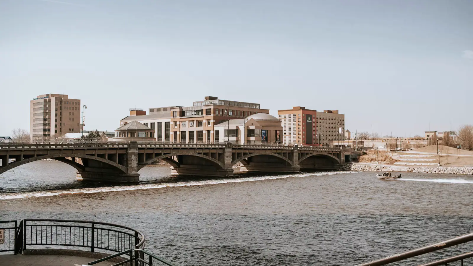 A pale stone museum building standing on a river bank beside a road bridge