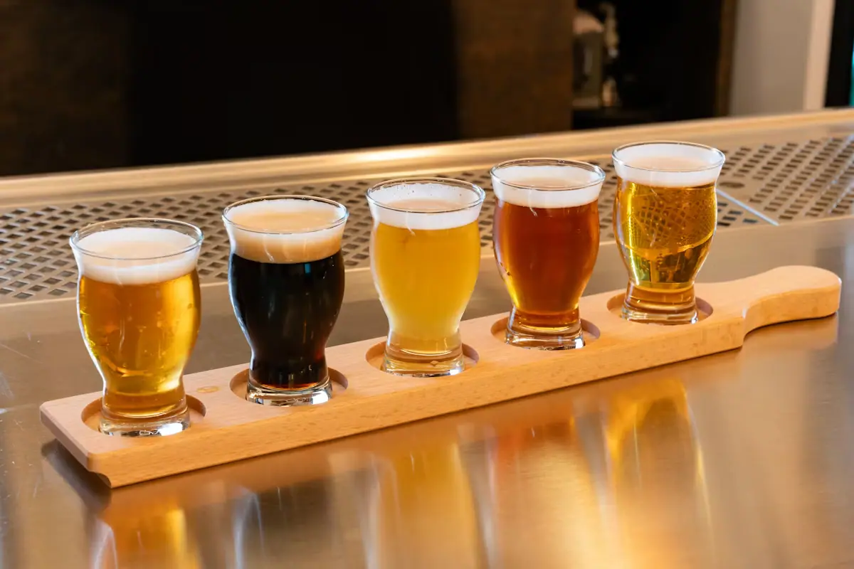 A row of small tasting glasses of beer lined up on a wooden serving tray