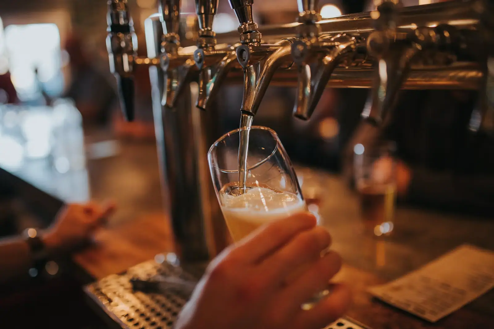 A bartender pulling a glass of beer from a row of taps along a brewery bar