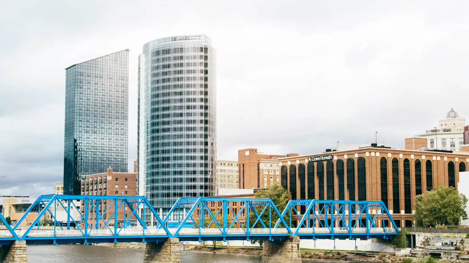 The blue steel truss of a former railroad bridge crossing the Grand River with downtown Grand Rapids behind it