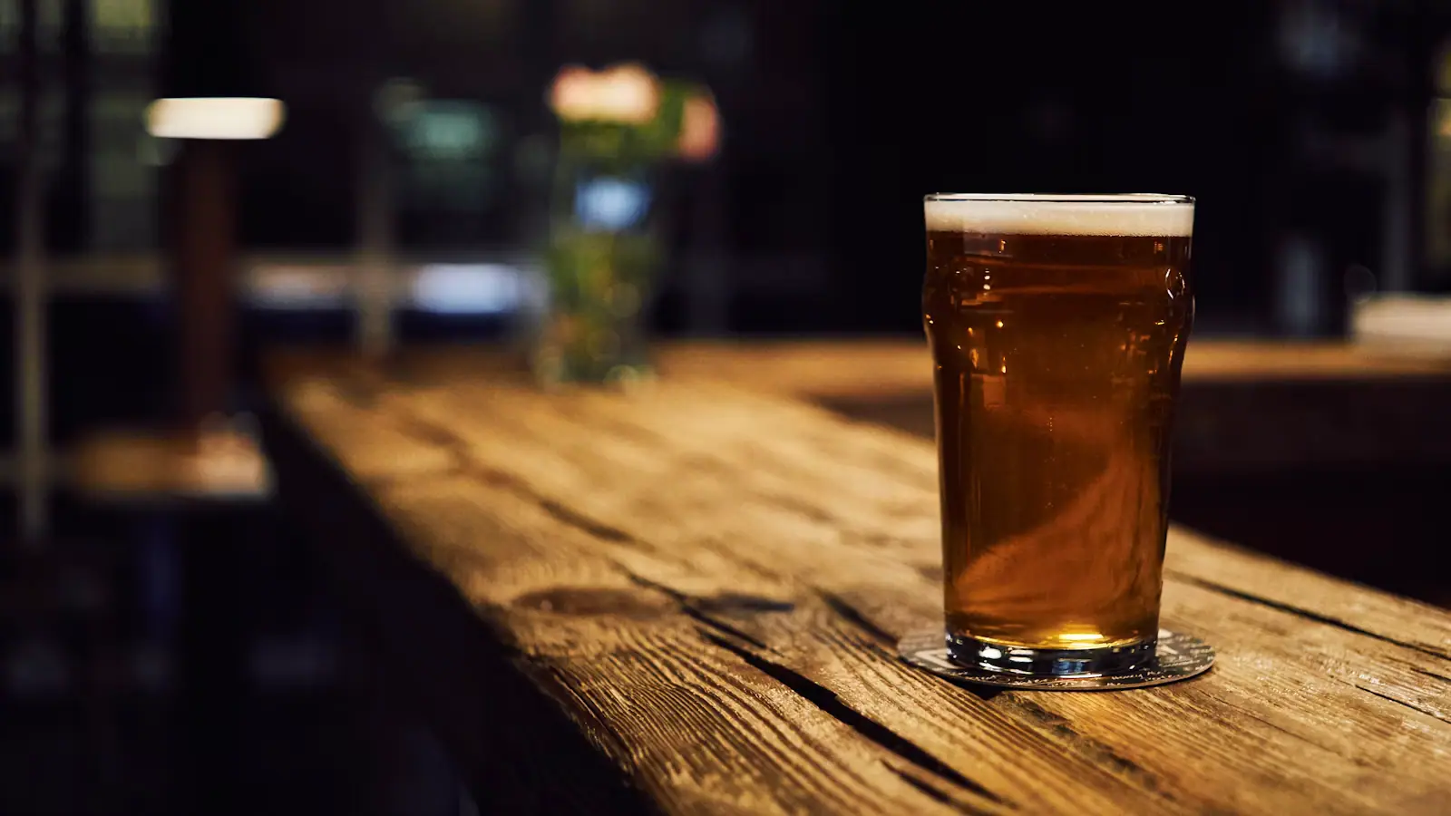 A row of tall beer glasses on a bar counter in front of brewery tanks