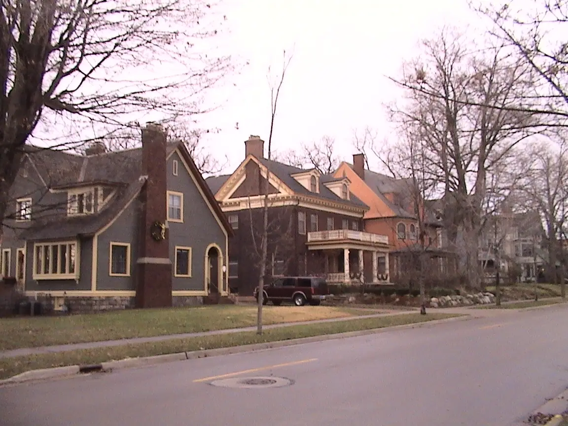 A large Victorian house with decorative trim behind a low fence on a residential street