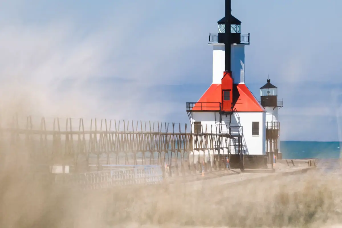 A red and white lighthouse standing at the end of a pier beside a sand beach