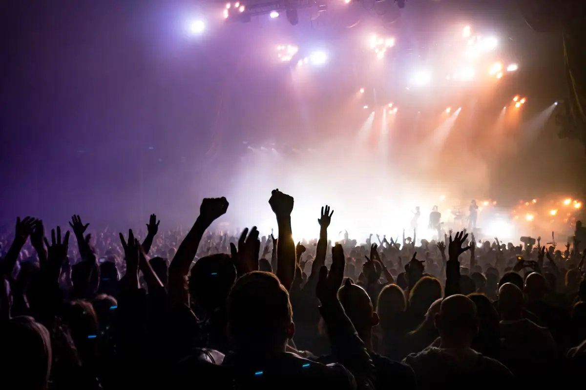 A crowd facing a brightly lit stage from the floor of a concert room