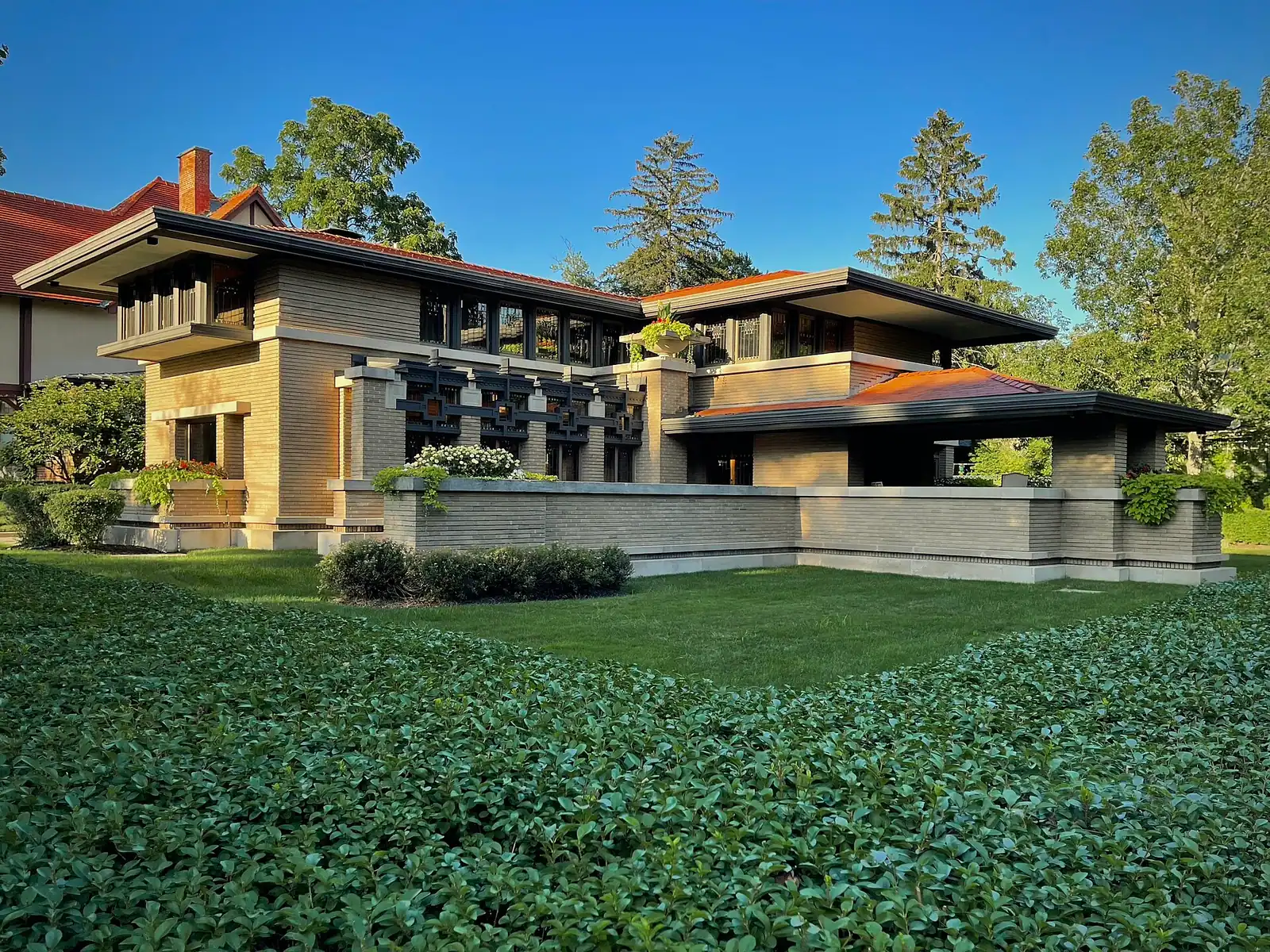 A low brick house with wide overhanging eaves set among mature trees