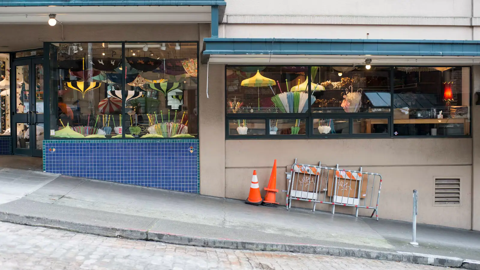 A small independent shopfront with plants and chairs on the pavement along a sloping street