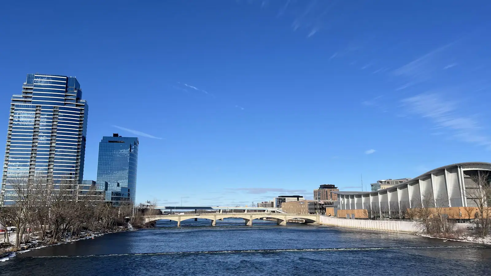 A wide river running between the low towers and brick blocks of a Midwestern downtown