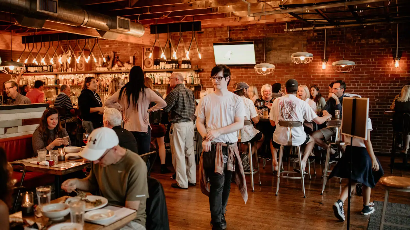 People sitting at long tables in a busy taproom with a bar behind them